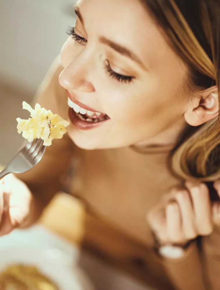 Donna che mangia la pasta con gusto, portando la forchetta alla bocca