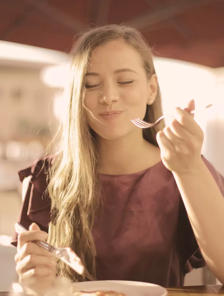 donna che assapora la pizza sorridendo ad occhi chiusi