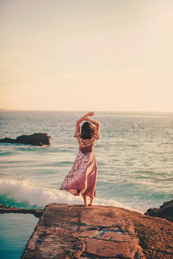 donna di spalle con le braccia alzate davanti al mare