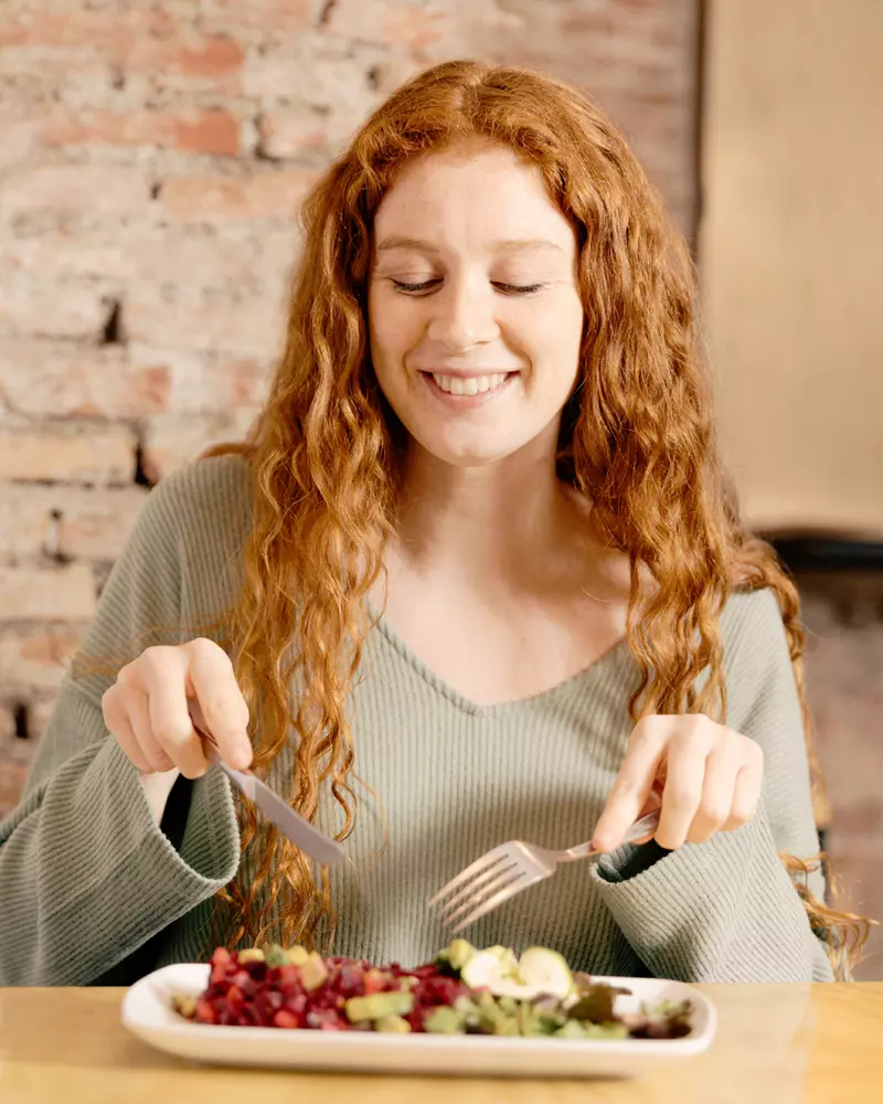 donna sorridente che sta per mangiare con le posate da un piatto